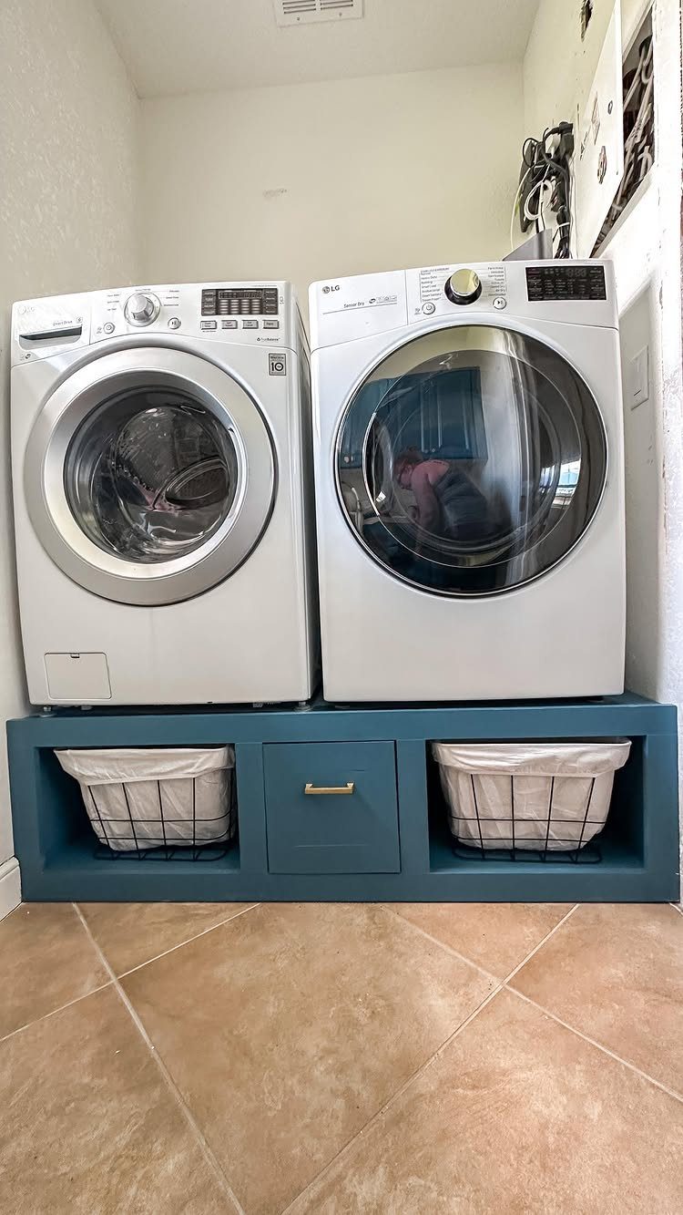 White washer and dryer on a teal storage pedestal with laundry baskets.