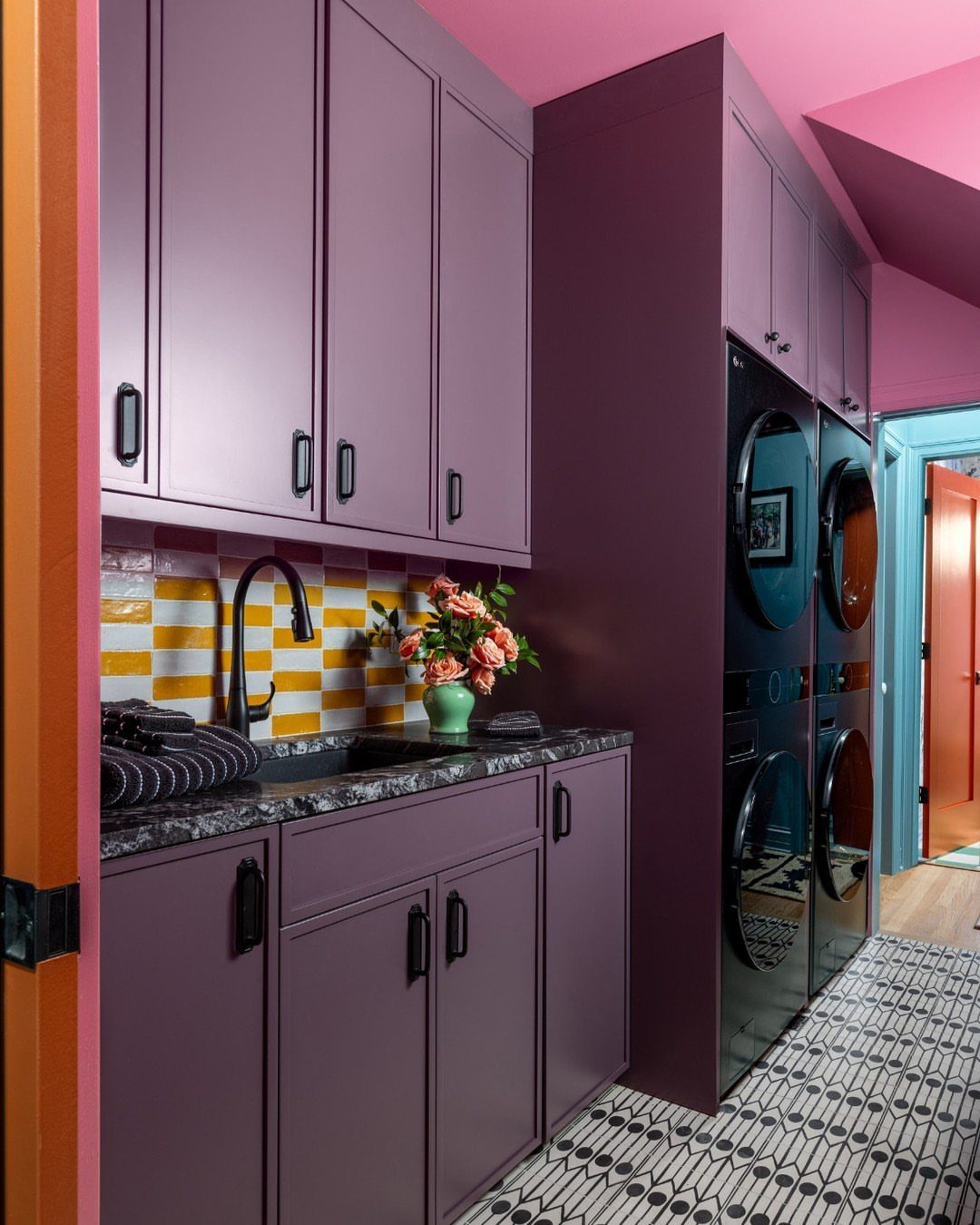 Purple laundry room cabinets and bright pink walls with yellow tiled backsplash.