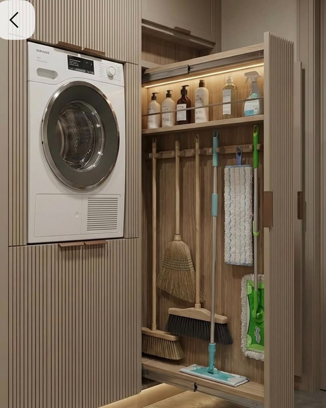 White washing machine and cleaning supply closet integrated into light wood cabinetry.