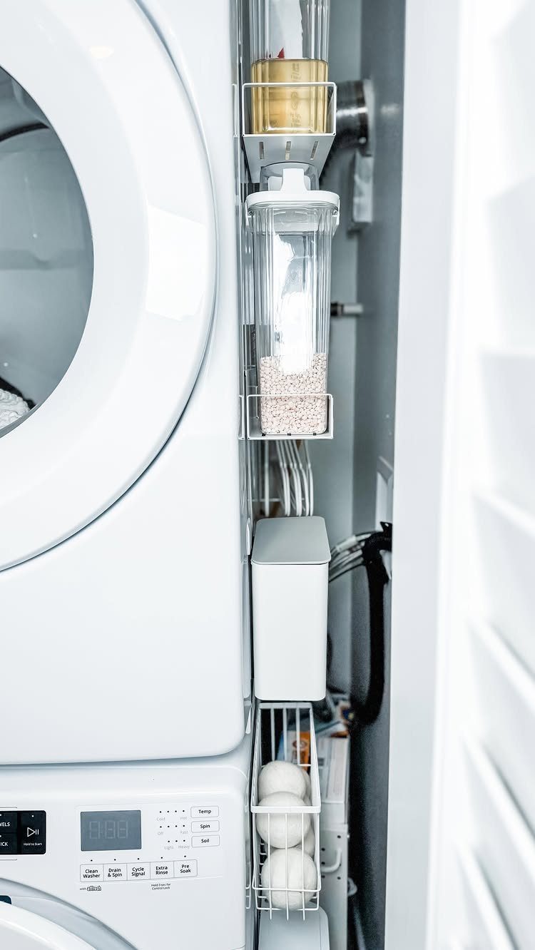 White stacked laundry machines with clear storage bins attached to the side.