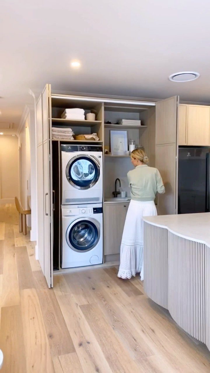 Woman standing in a modern laundry closet with stacked washer and dryer units.