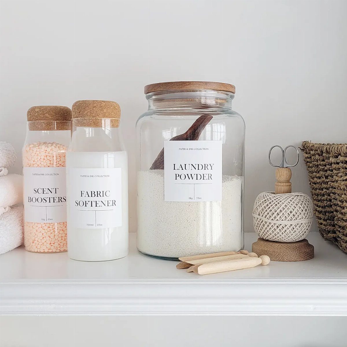 Glass jars with cork lids holding laundry powder and softener on white shelf