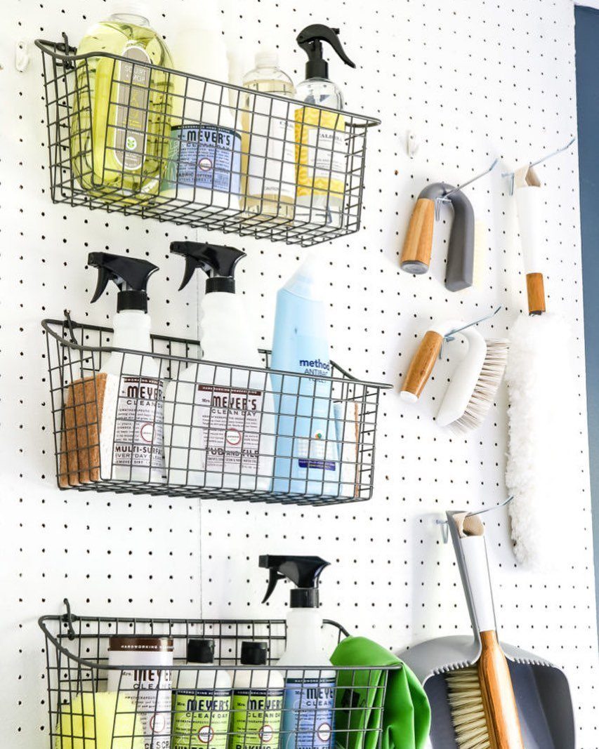 White pegboard with black wire baskets holding cleaning supplies and hanging brushes.