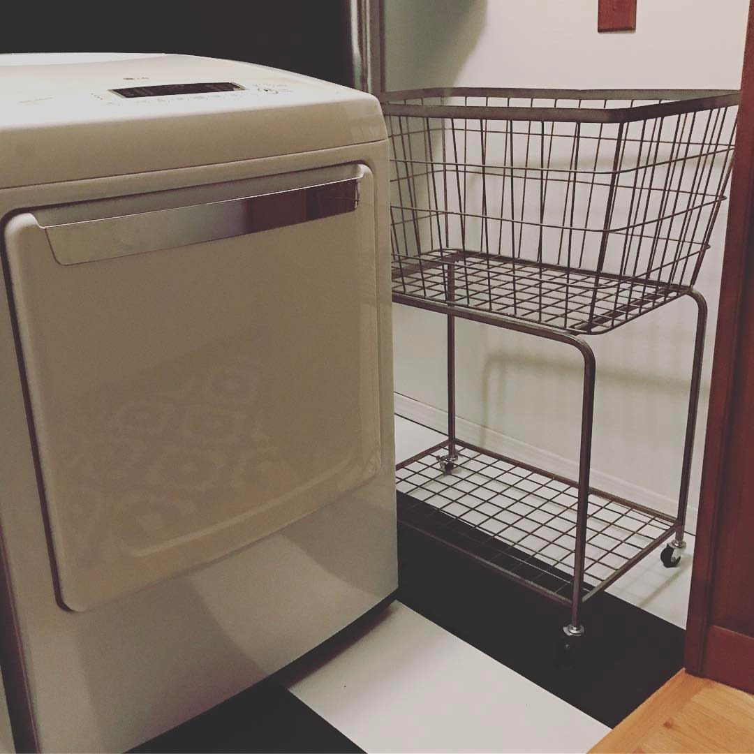White washing machine next to a two-tier metal wire rolling storage cart.