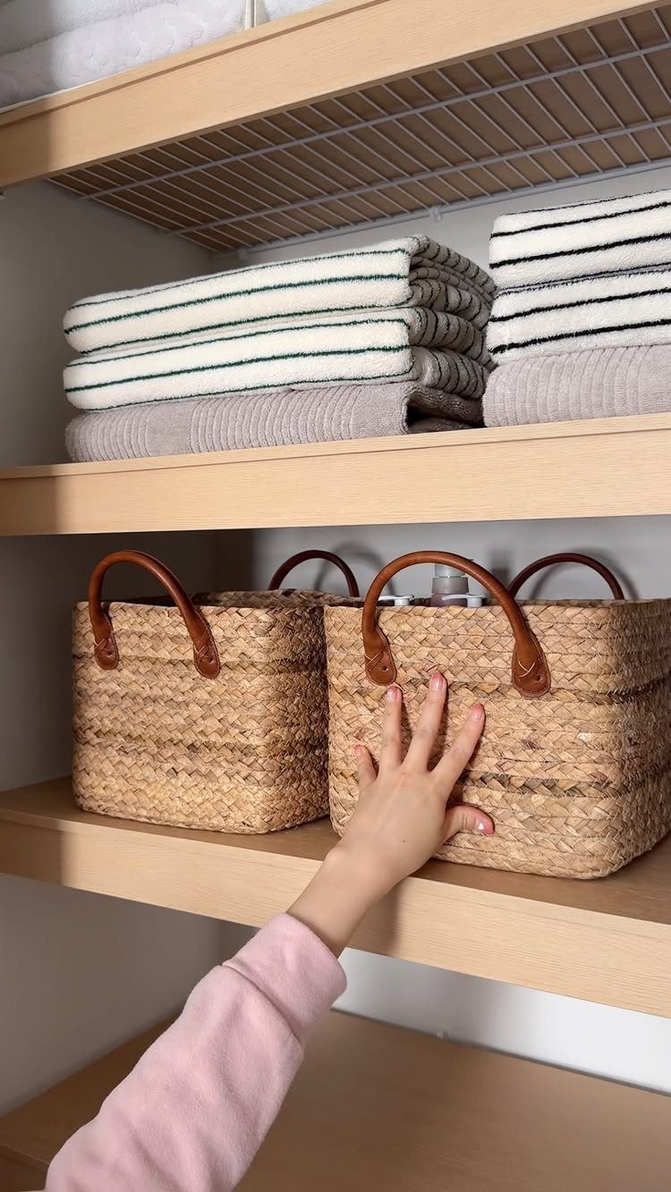 Woven wicker baskets and folded towels organized on light wood laundry room shelves.