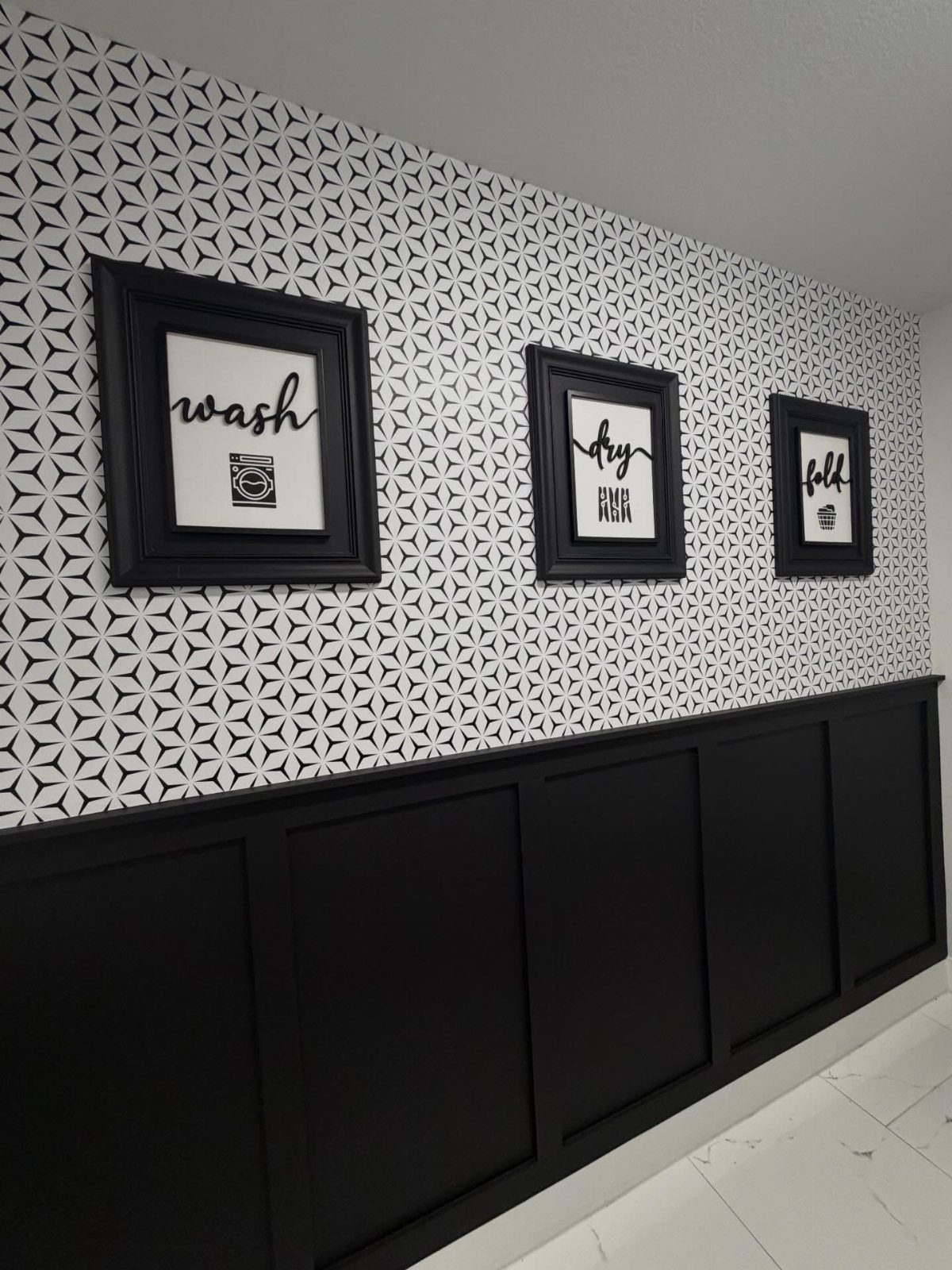 Black and white geometric wallpaper above black wainscoting with laundry-themed framed art.