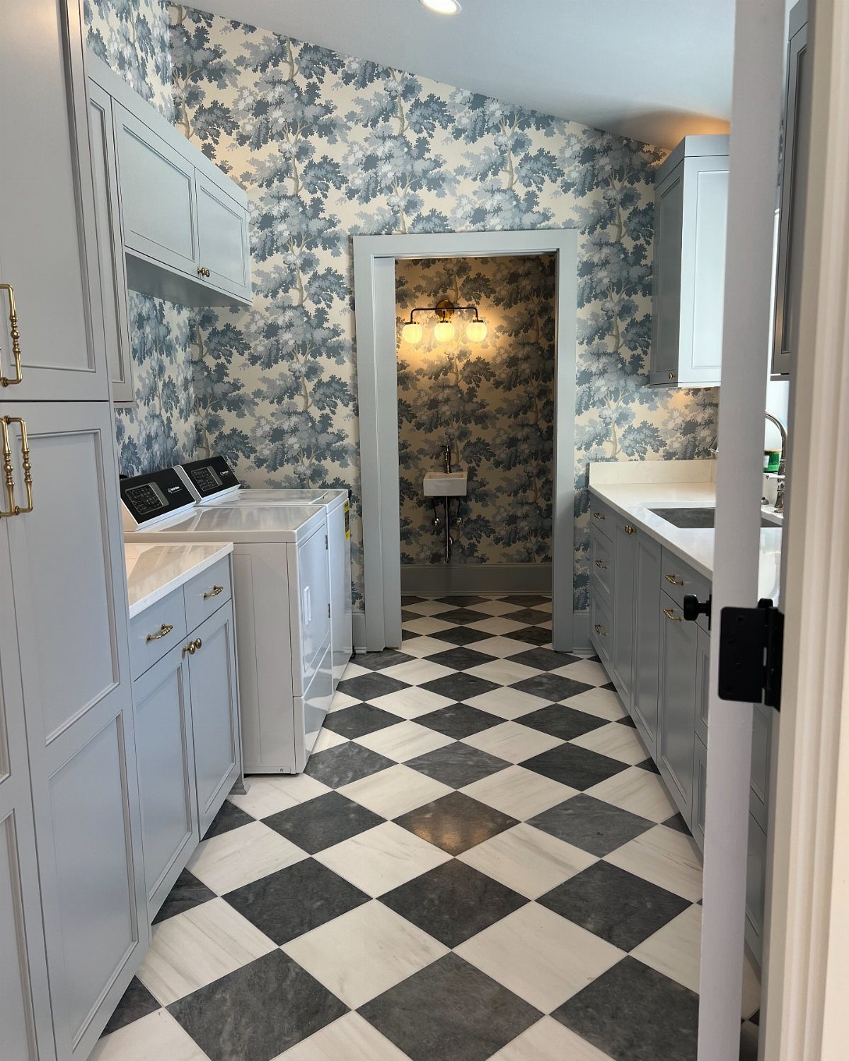 Laundry room with blue landscape wallpaper and black and white checkered tile flooring