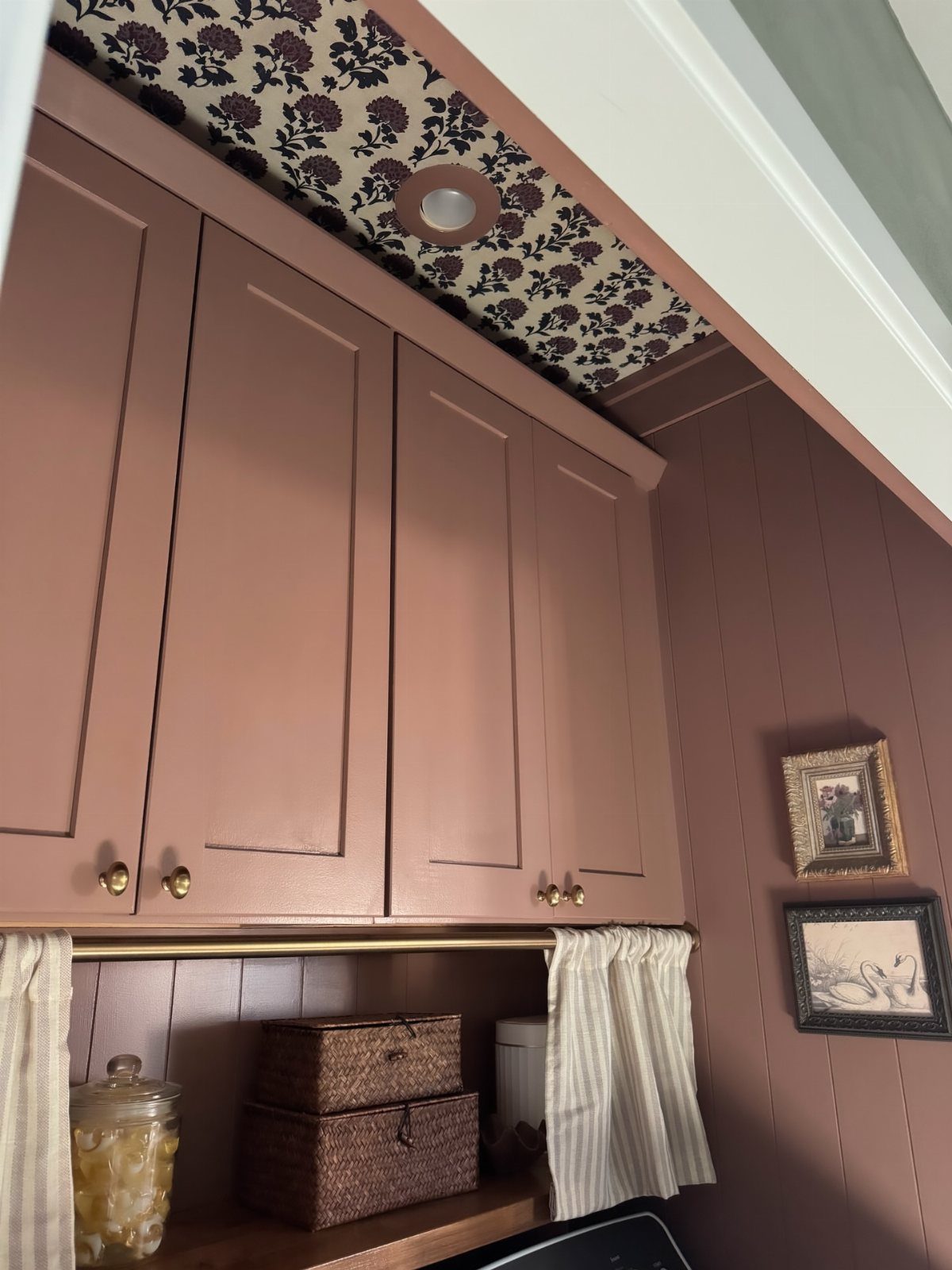 Floral patterned wallpaper on the ceiling of a laundry room with mauve cabinets.