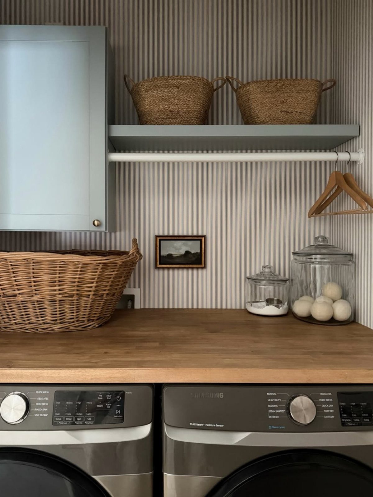 Laundry room with grey pinstripe wallpaper, wooden countertop, and wicker storage baskets.