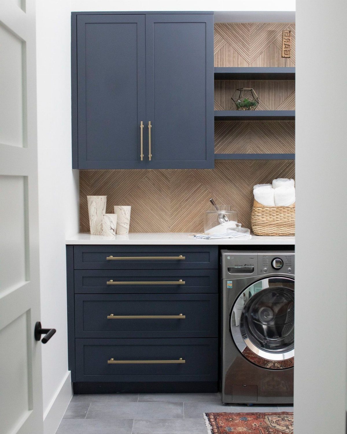 Navy blue laundry cabinets with a light brown chevron patterned wallpaper backsplash.