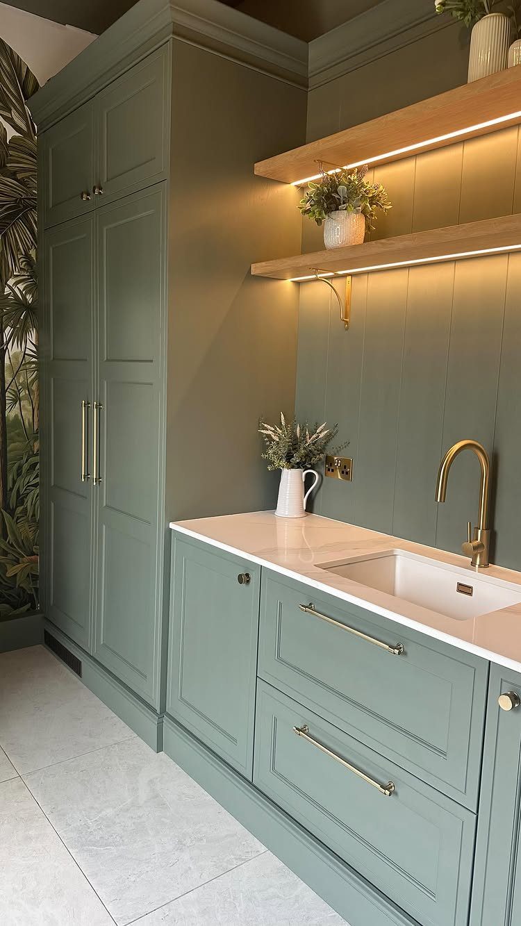 Sage green laundry room cabinets with white countertops and tropical leaf wallpaper.
