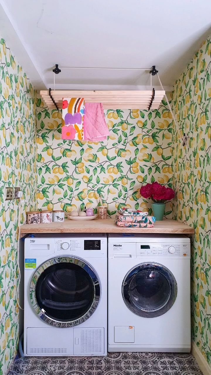 Small laundry room with lemon patterned wallpaper and two white washing machines.