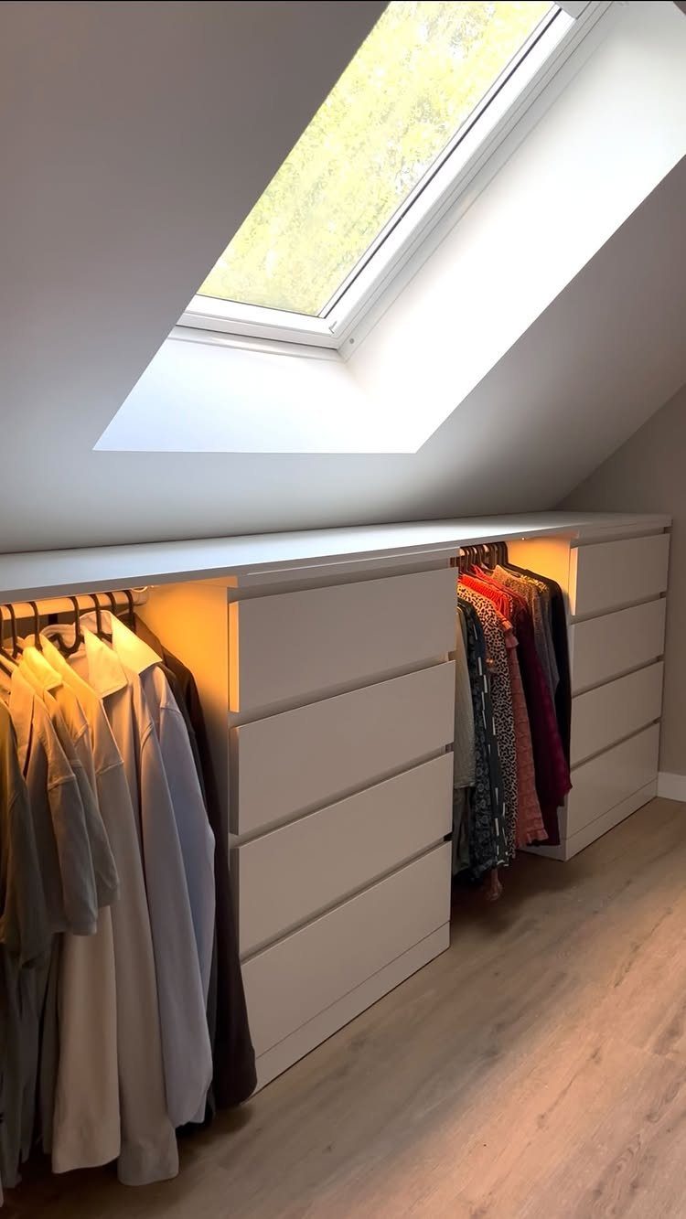 White built-in closet with drawers and hanging clothes under a sloped attic ceiling.