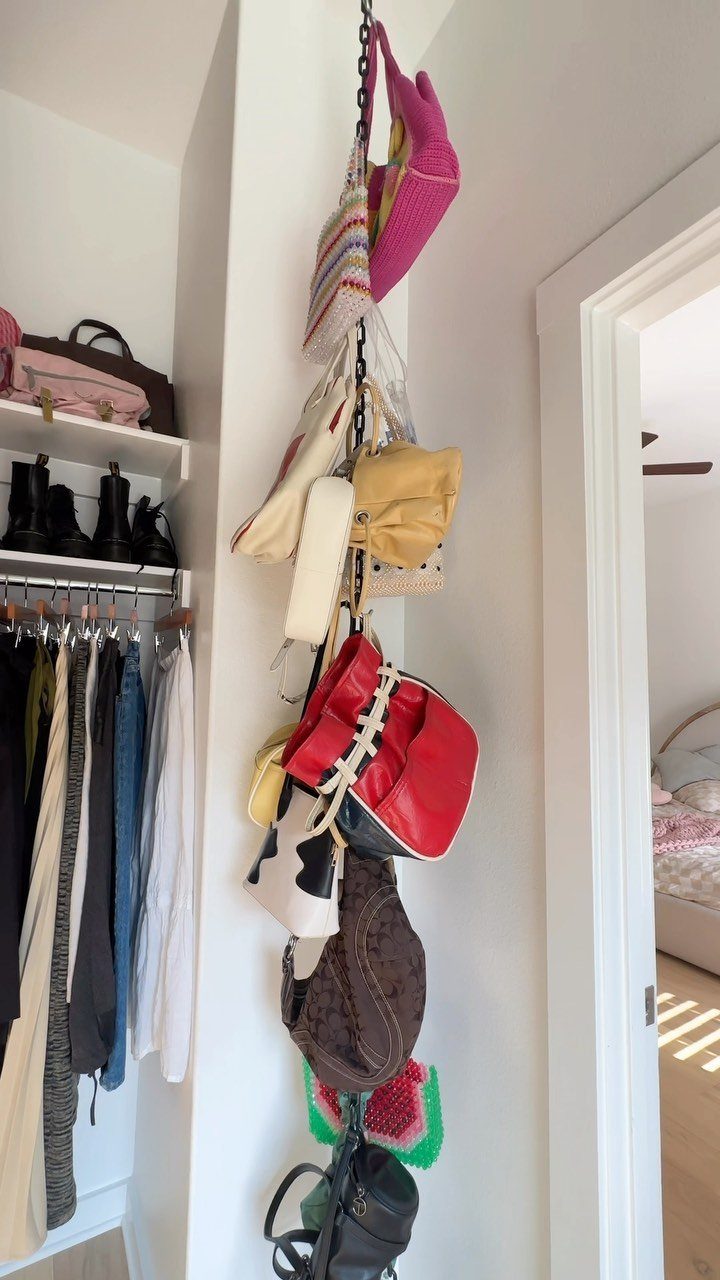 Handbags hanging from a vertical chain attached to a white wall in a closet.