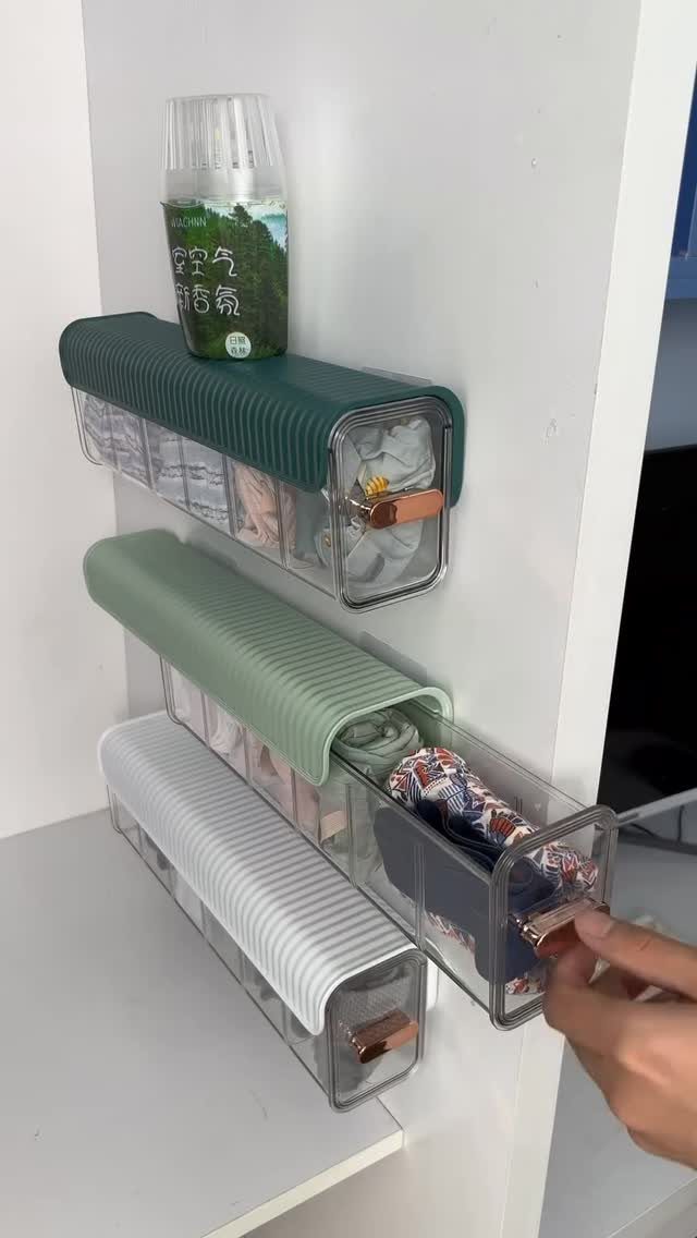 Clear plastic storage bins with fabric covers mounted on a white wall holding clothes.
