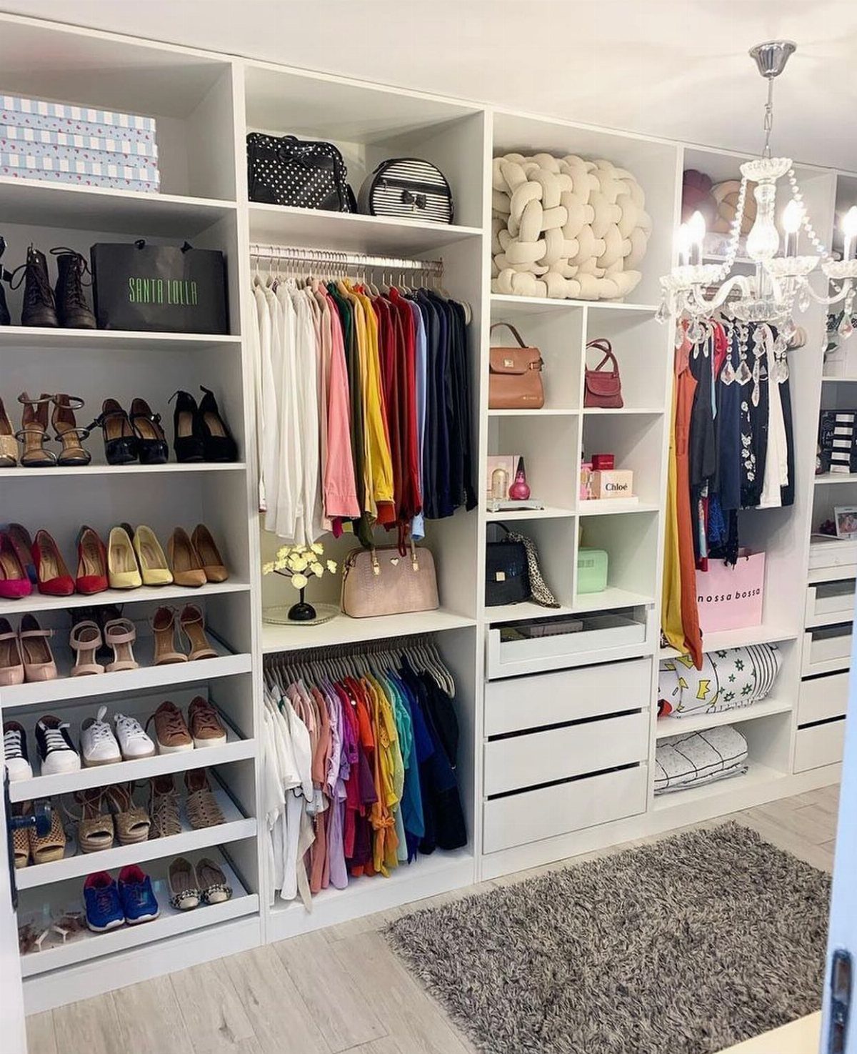 White closet system with clothes organized by color and shelves of shoes.