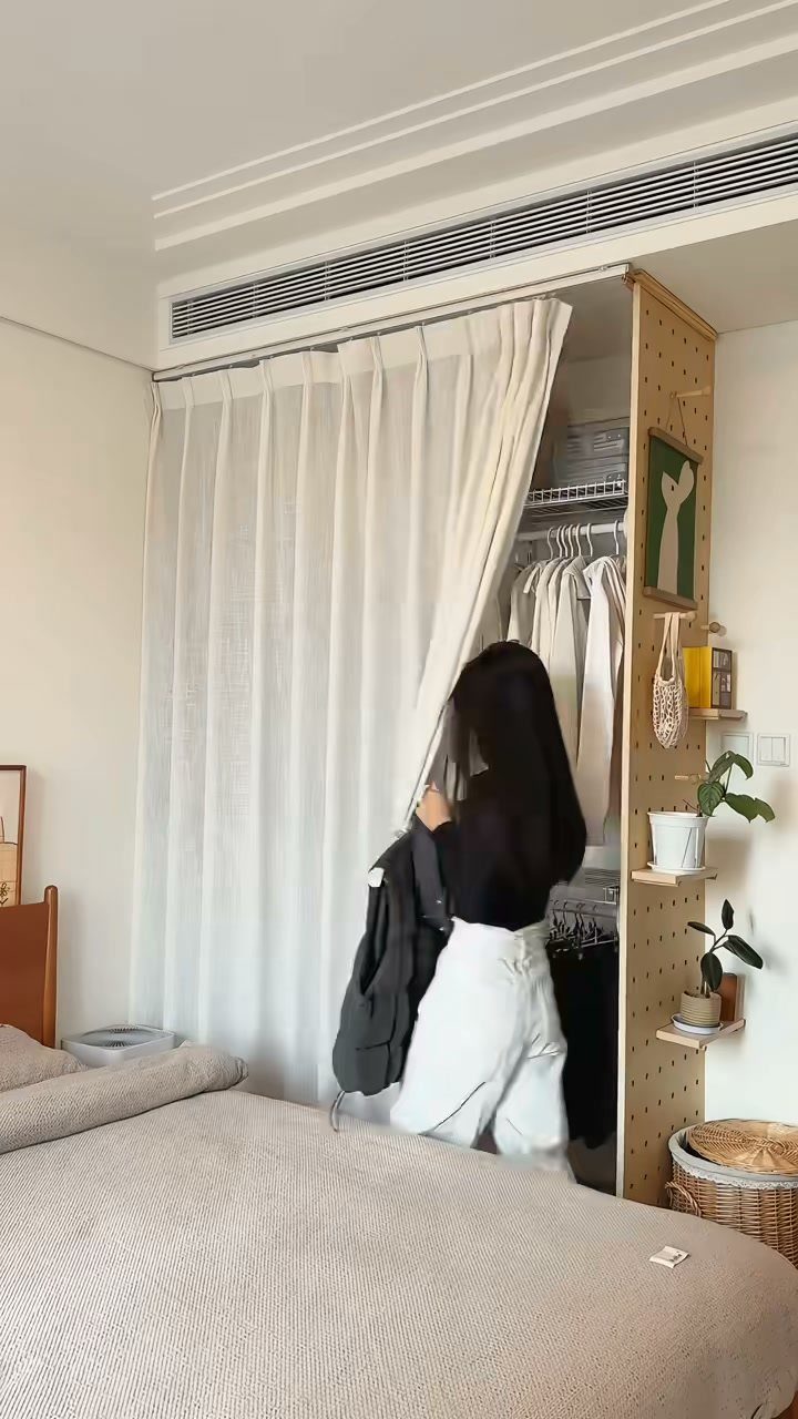 Woman standing by a custom closet system with white curtains and wooden pegboard.