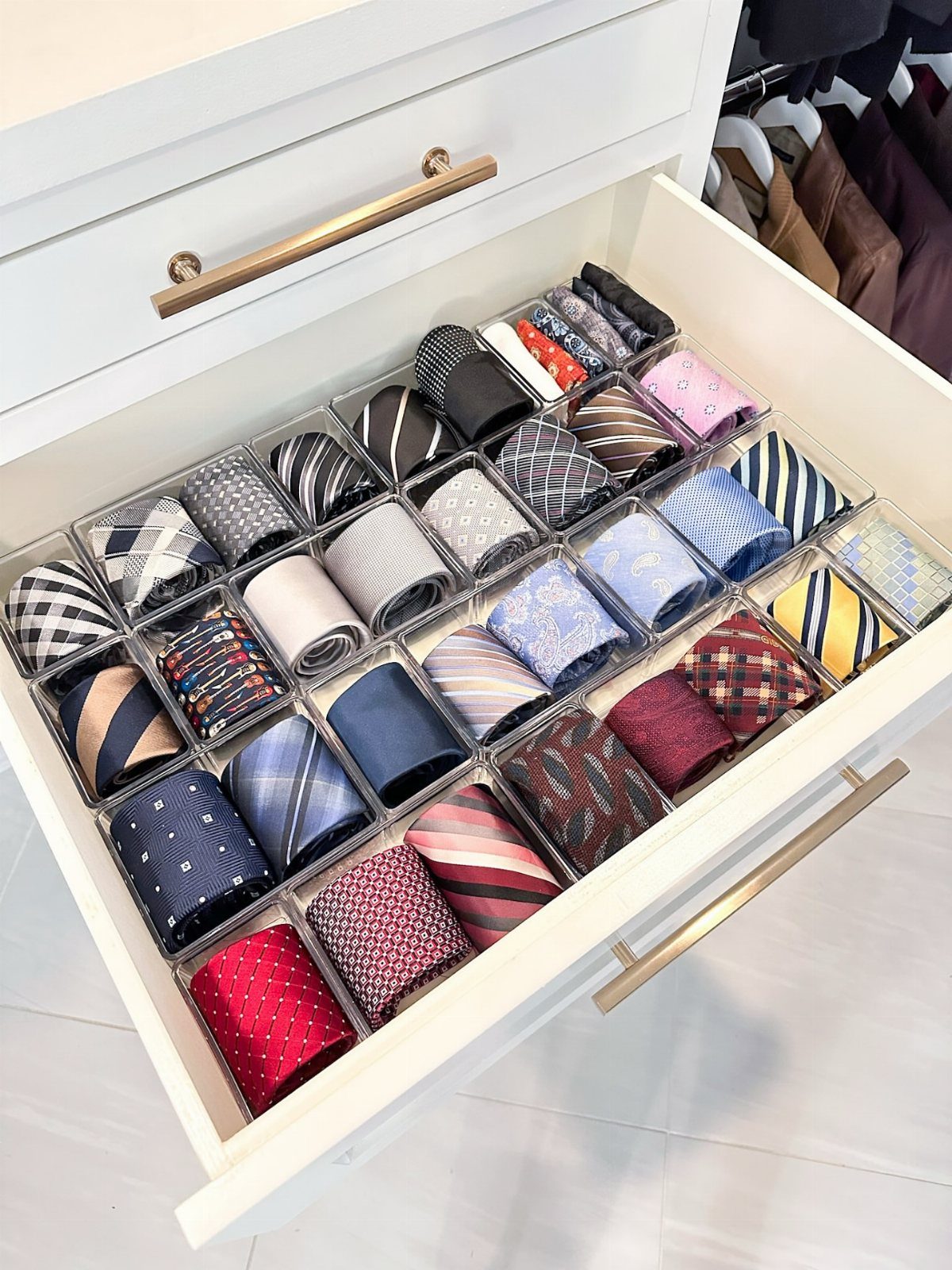 Rolled neckties organized in clear acrylic dividers inside a white dresser drawer.