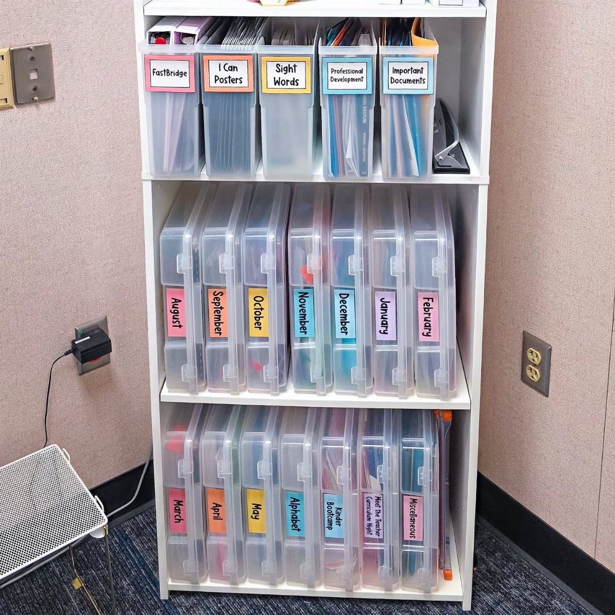 White shelving unit with clear plastic bins and colorful labels for organization.