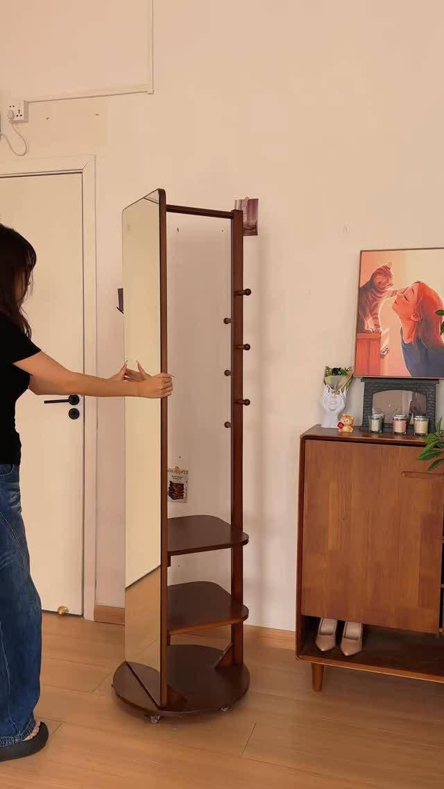 Rotating wooden storage unit with mirror and shelves in a bright room.