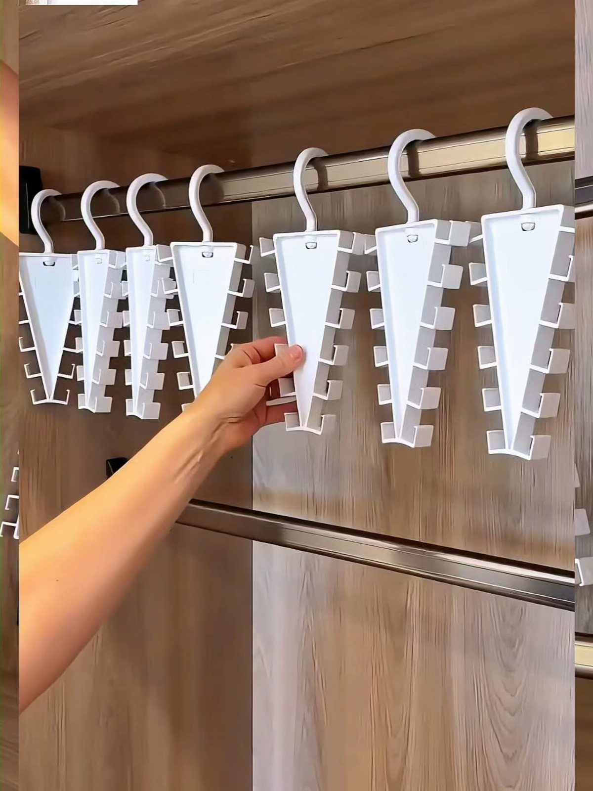 White multi-layered space-saving hangers hanging on a rod in a wooden closet.