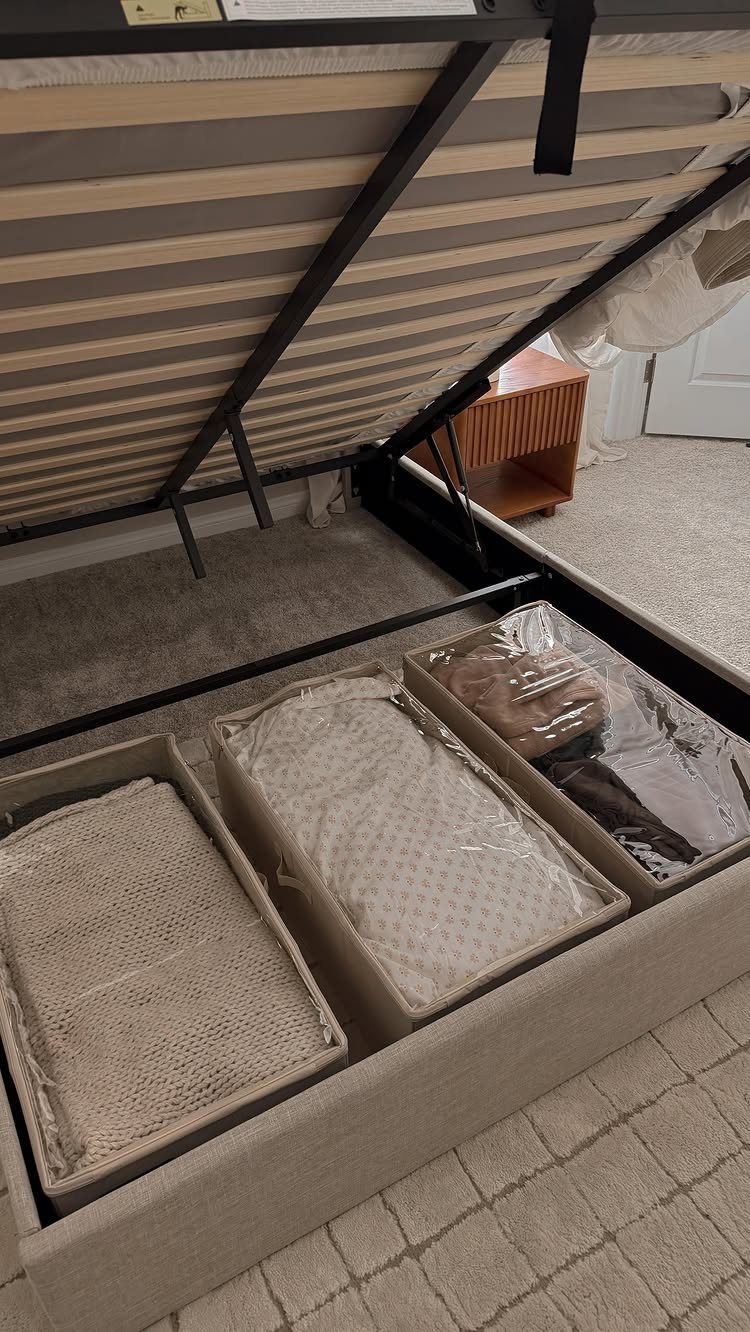 Storage bins with folded linens tucked into a compartment under a bed frame.