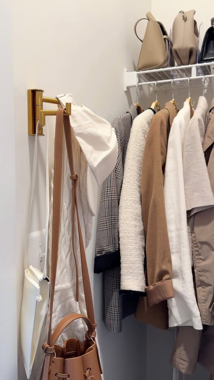 Gold wall hook holding bags next to a rack of neutral colored clothing.
