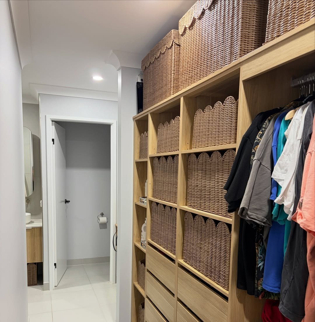 Woven wicker baskets stored in light wood closet cubbies next to hanging clothes.