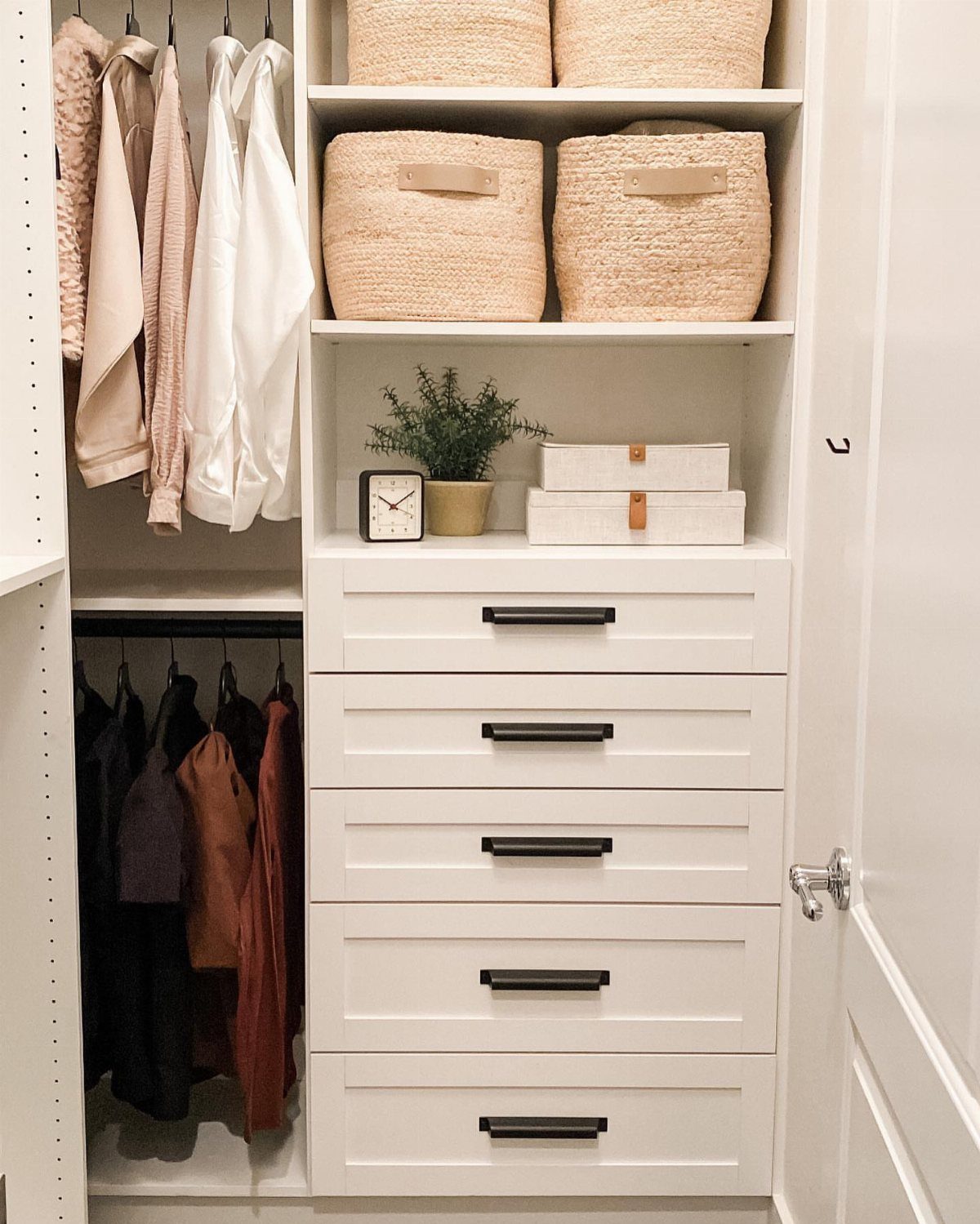 White built-in closet shelving with woven baskets, drawers, and hanging clothes.