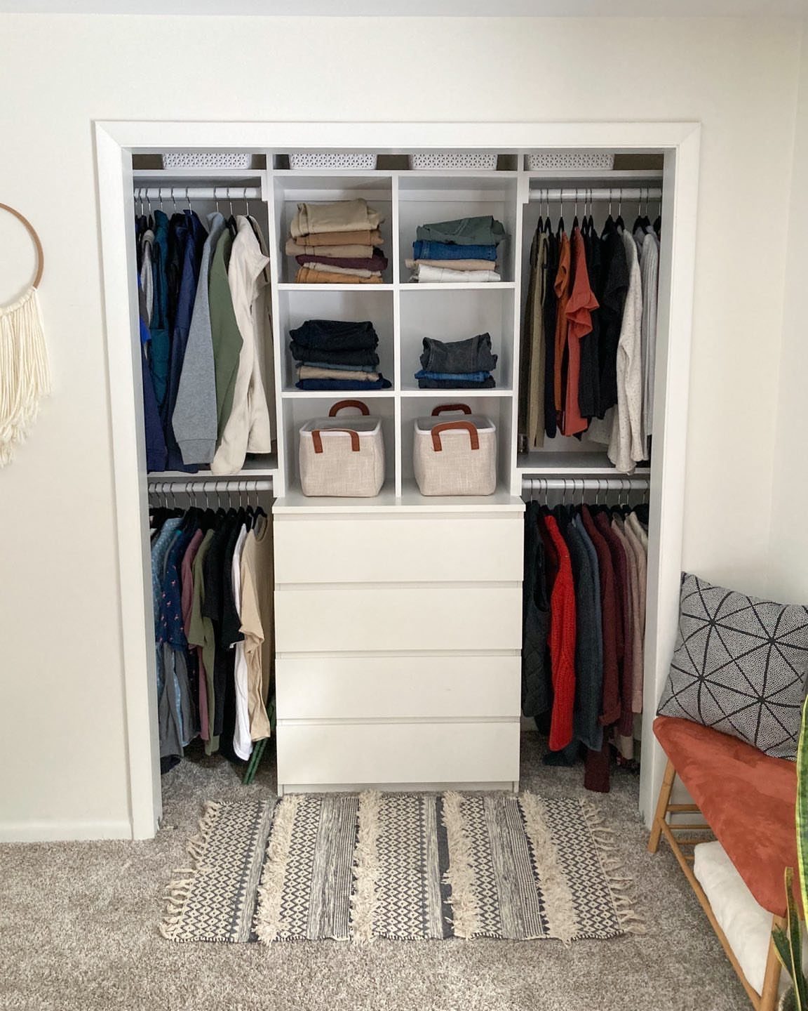 White walk-in closet with hanging clothes, open shelving, and a central drawer unit.