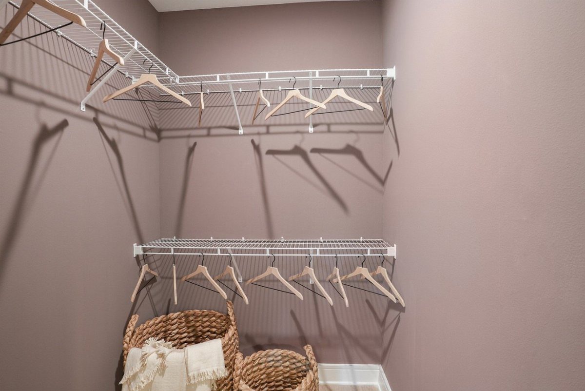 White wire double hanging rods with wooden hangers in a mauve walk-in closet.