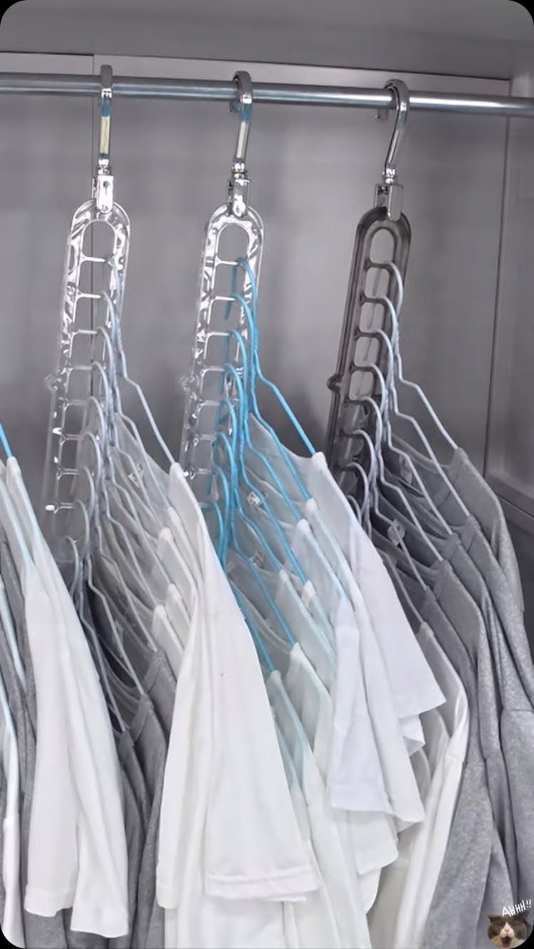 Multi-layered hangers holding white and grey t-shirts in a grey walk-in closet.