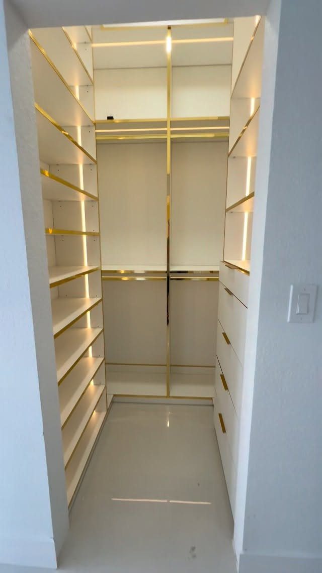 Modern white walk-in closet with gold accents and integrated LED lighting on open shelves