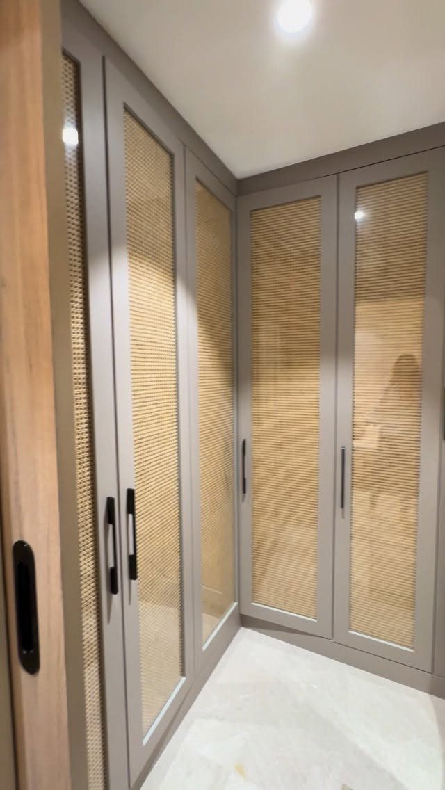 Grey wardrobes with rattan panels in a small walk-in closet with marble floors.
