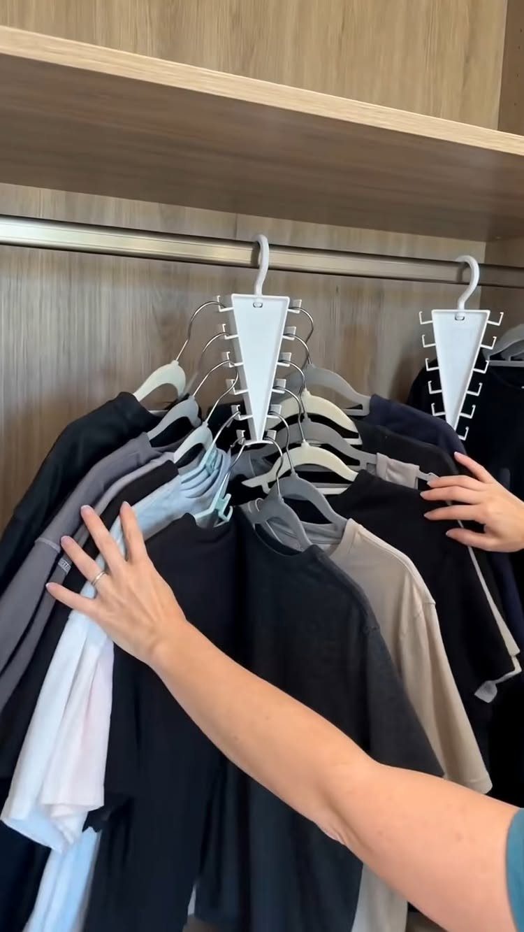 Multi-layered white hanging organizers holding t-shirts on a metal closet rod.