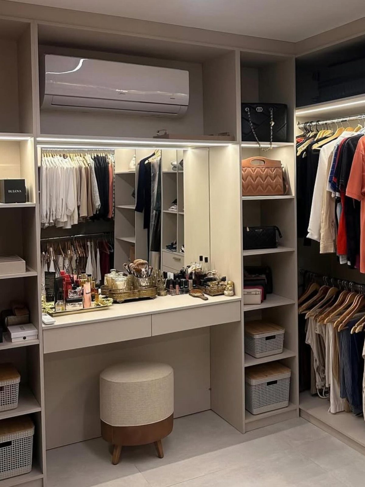 Makeup vanity with mirror and ottoman integrated into a beige walk-in closet system.