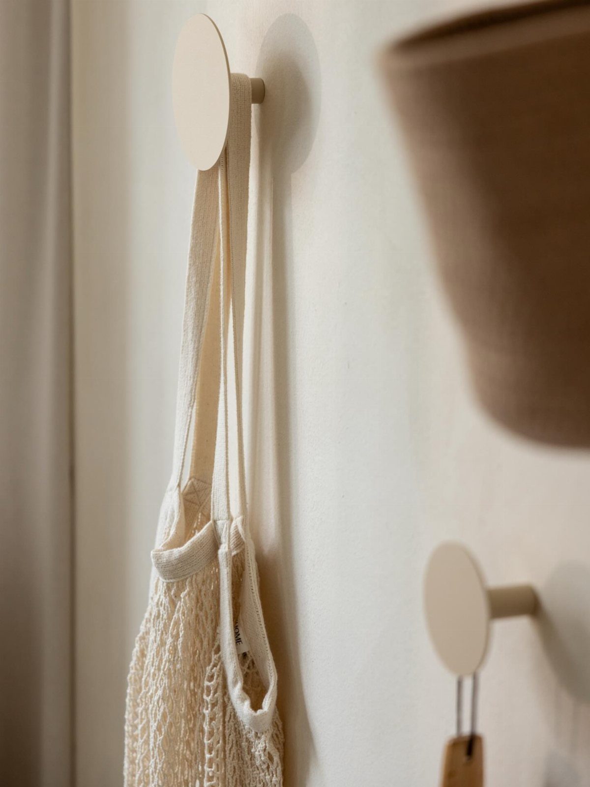 Beige round wall hooks holding a cream mesh bag on a white wall.