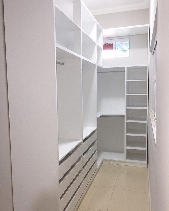 White built-in closet system with shelves, drawers, and hanging rods in a small room.
