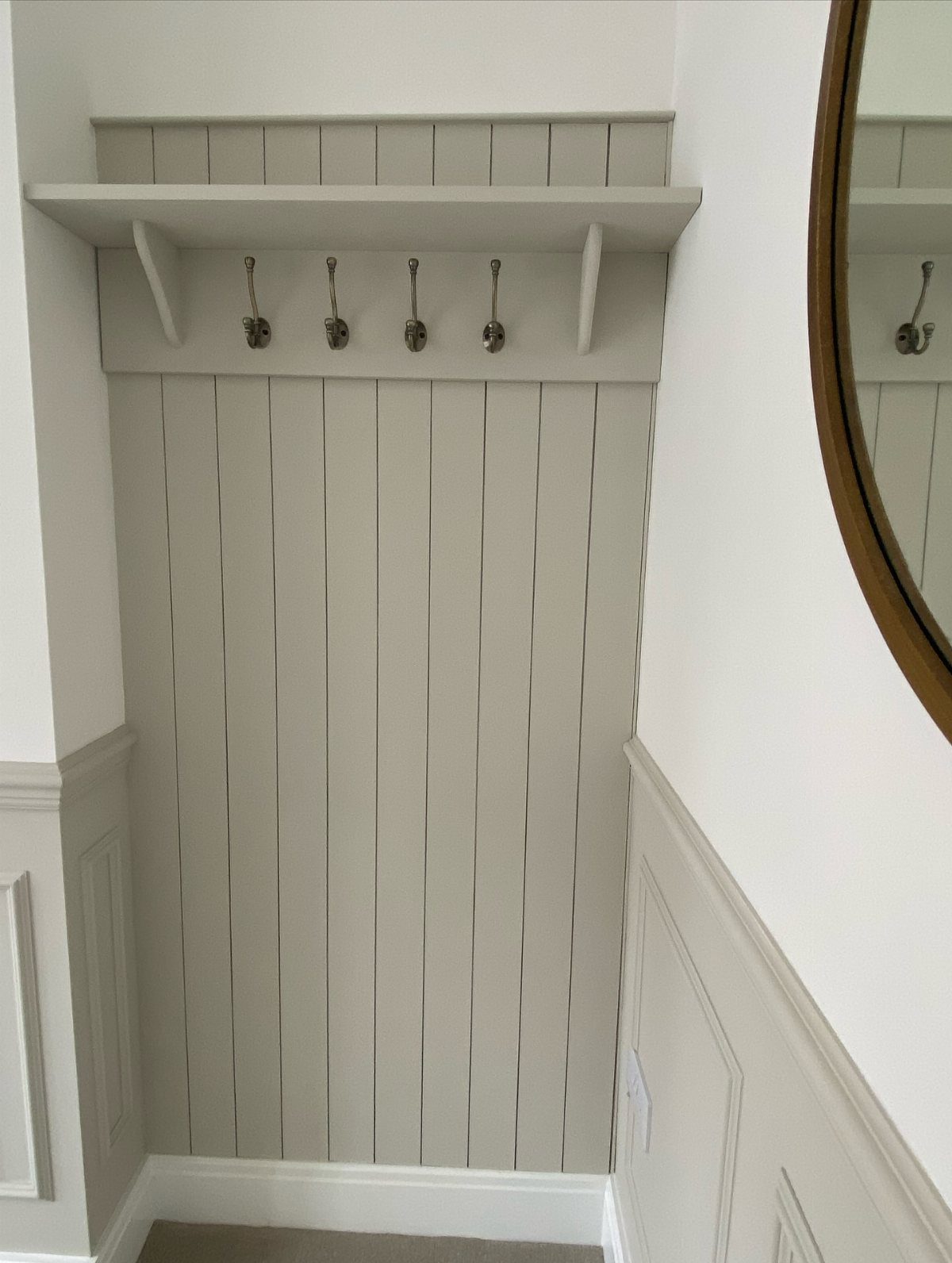 Silver metal hooks mounted under a grey wooden shelf on a paneled wall.