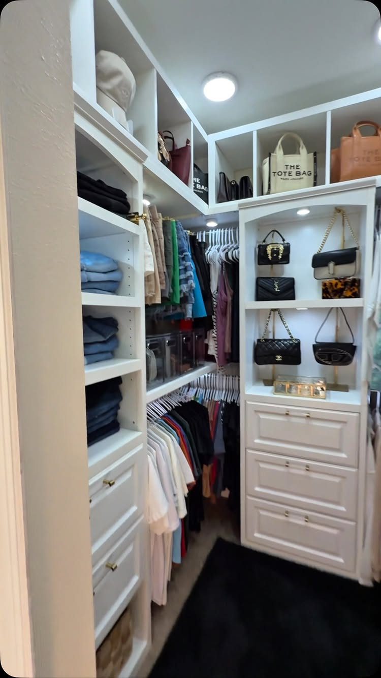 Small walk-in closet with white shelving, hanging clothes, and organized handbags.