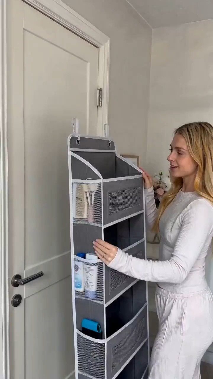 Woman organizing toiletries in a grey hanging pocket organizer on a white door.