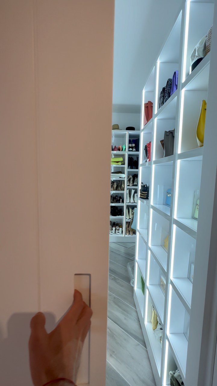 White built-in closet shelving with integrated LED lighting holding bags and accessories.
