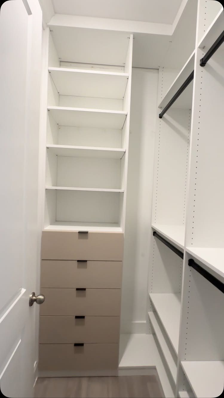 Small walk-in closet with white shelving, beige drawers, and black hanging rods.