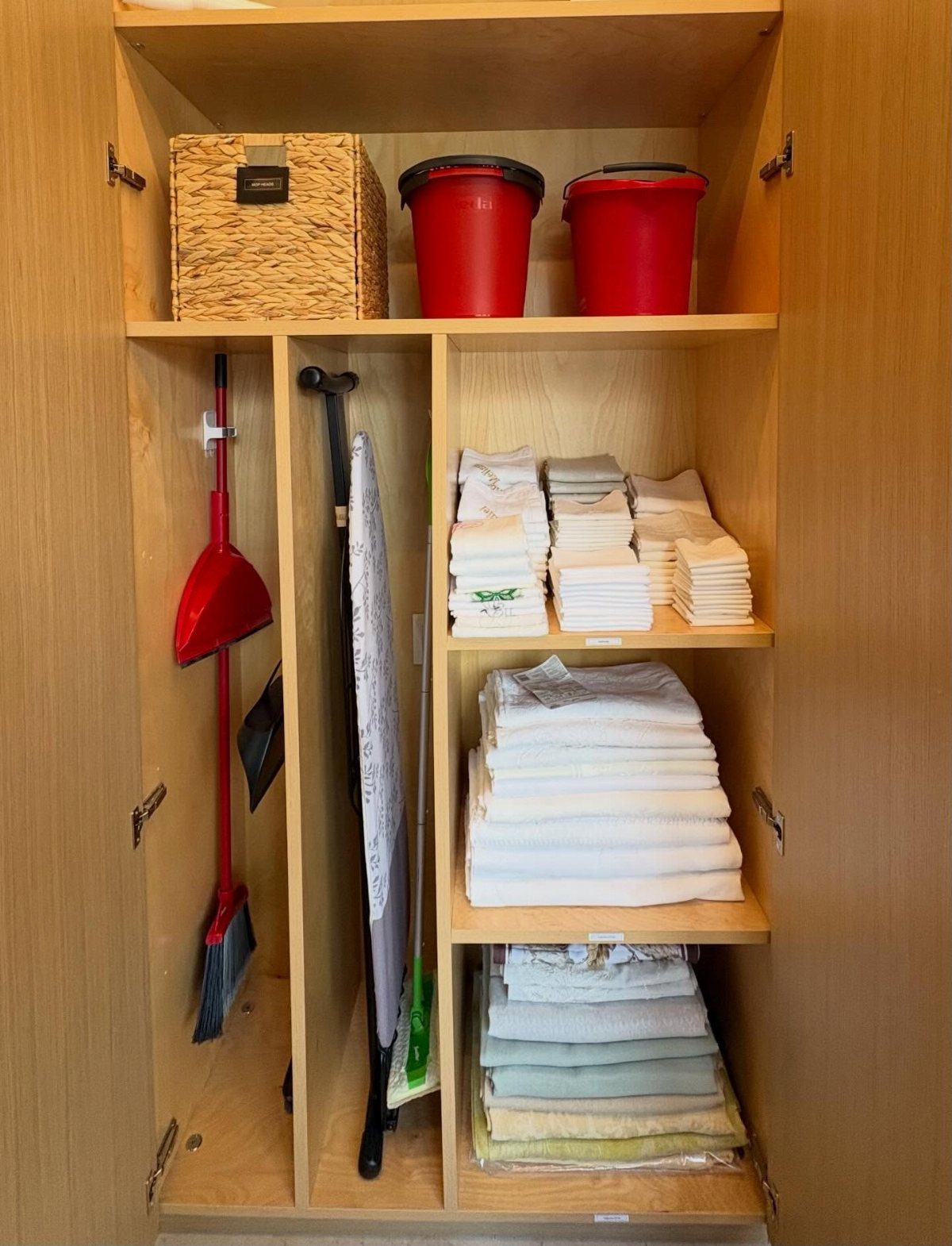 Woven basket and red buckets stored on the top shelf of a wooden closet.