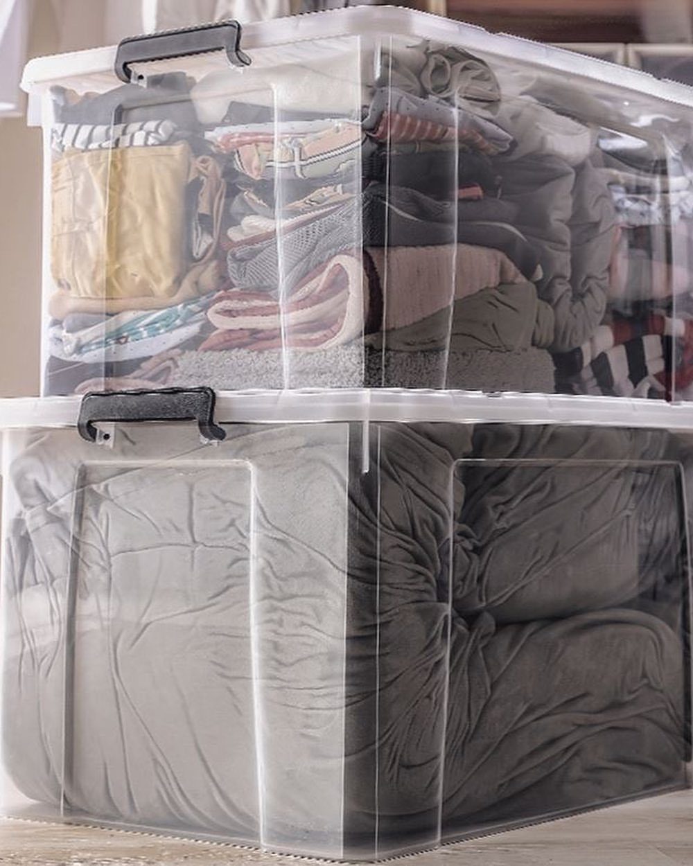 Clear plastic storage bins stacked and filled with neatly folded colorful clothing.