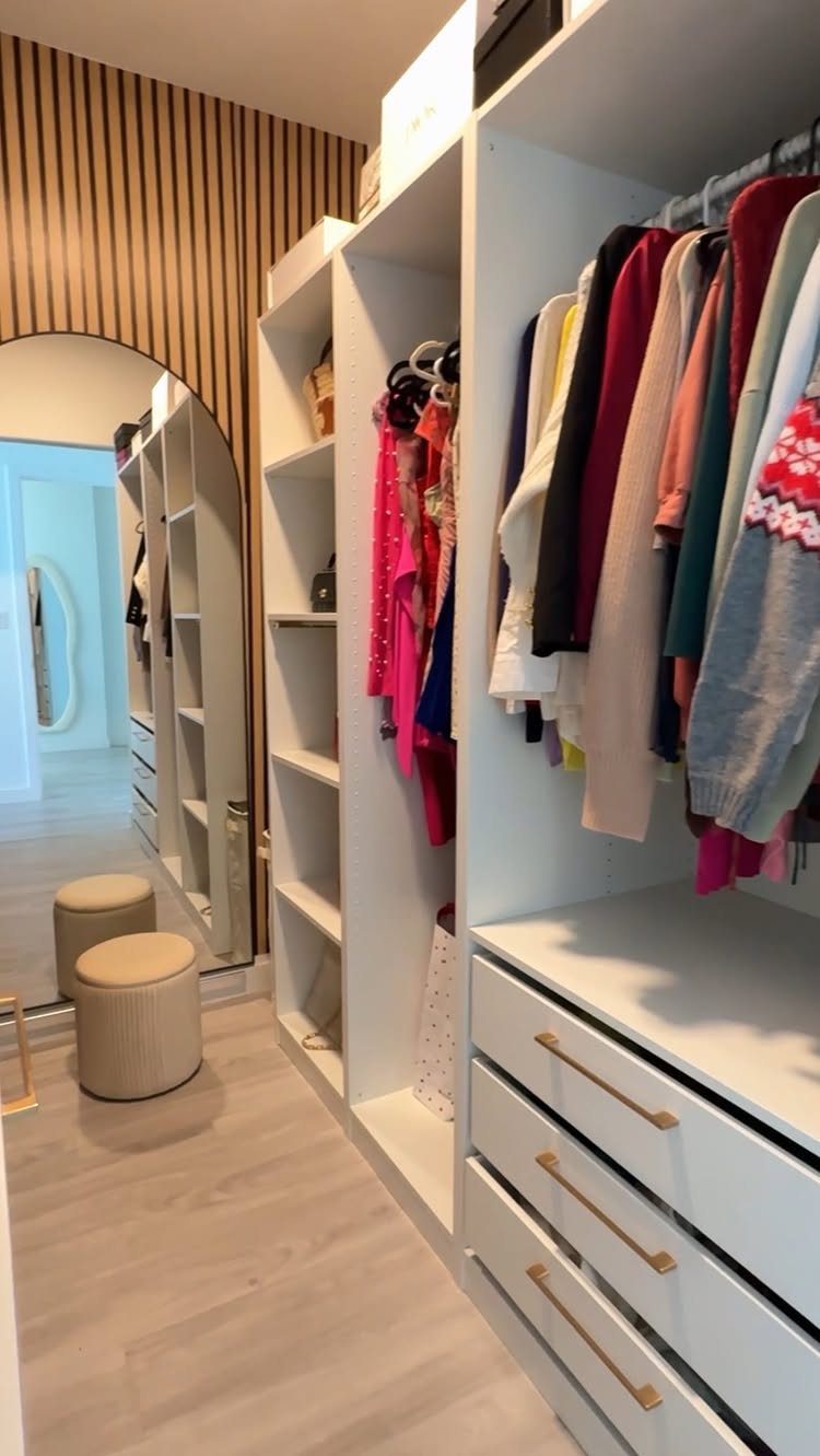 White custom closet system with hanging clothes, drawers, and an arched mirror.