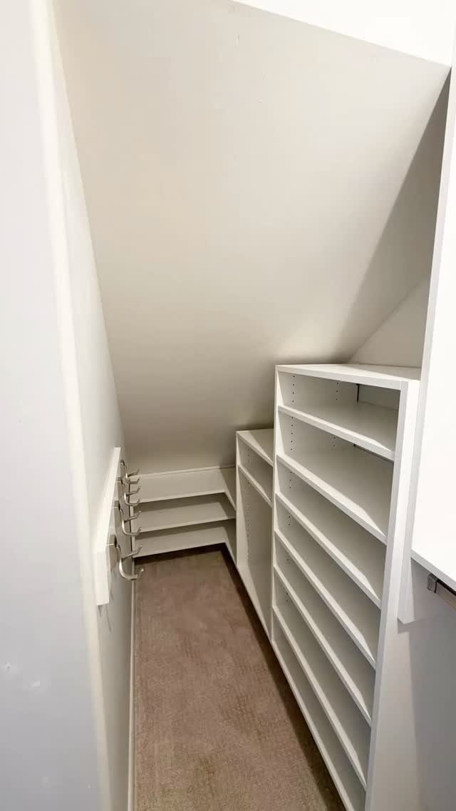 White built-in shelving units in a narrow walk-in closet with a sloped ceiling.