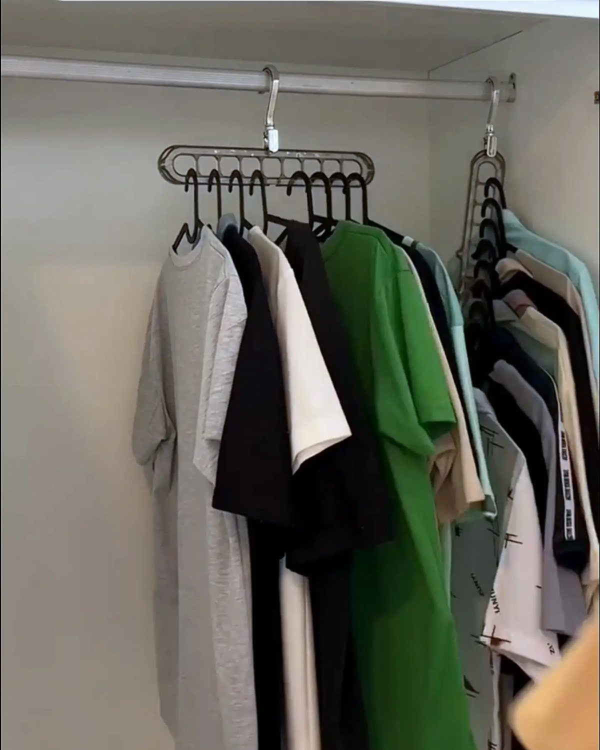 Thin black hangers holding colorful t-shirts on a white closet rod.