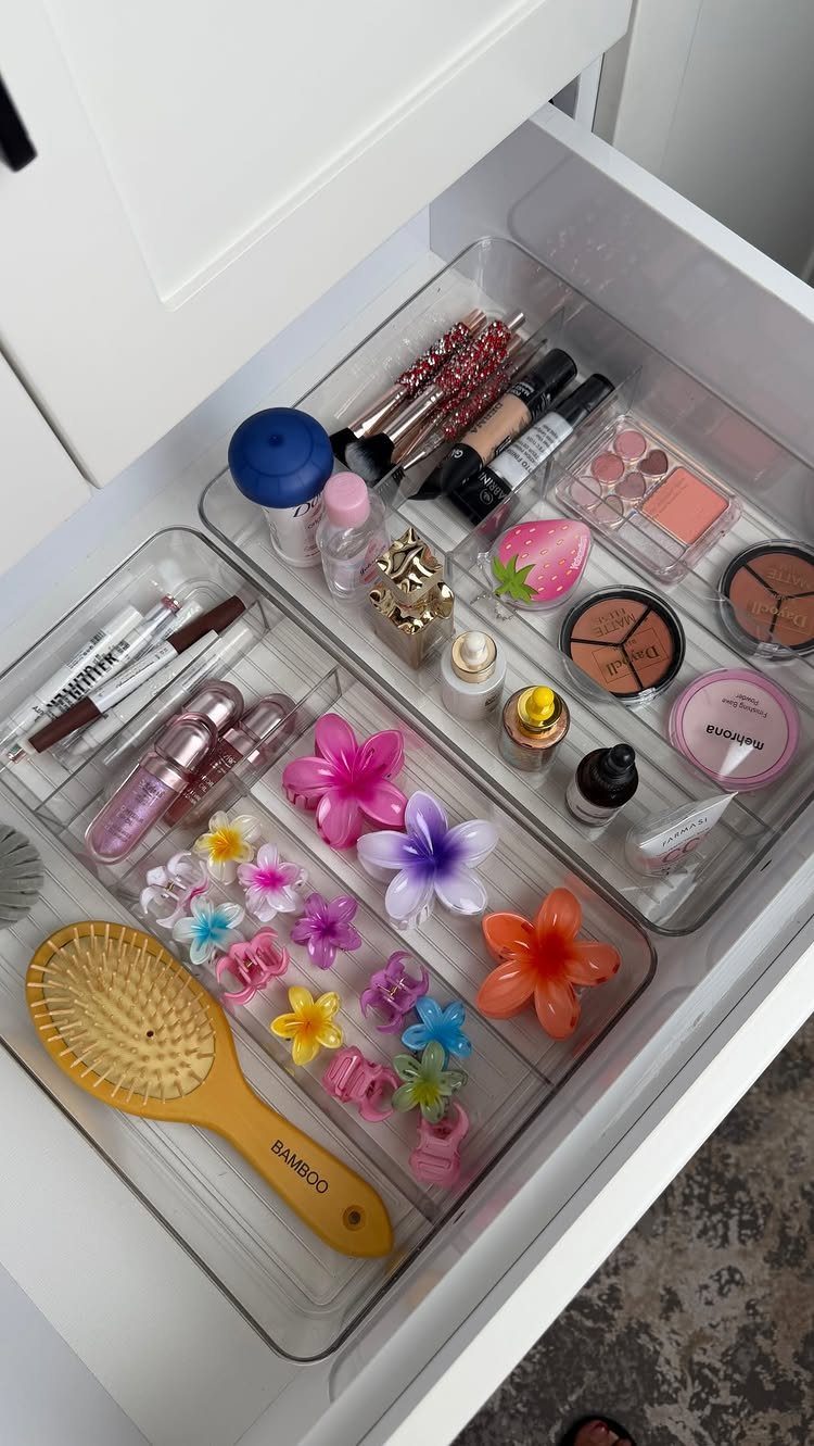 Clear acrylic drawer dividers organizing makeup, skincare, and colorful hair clips in a white drawer.