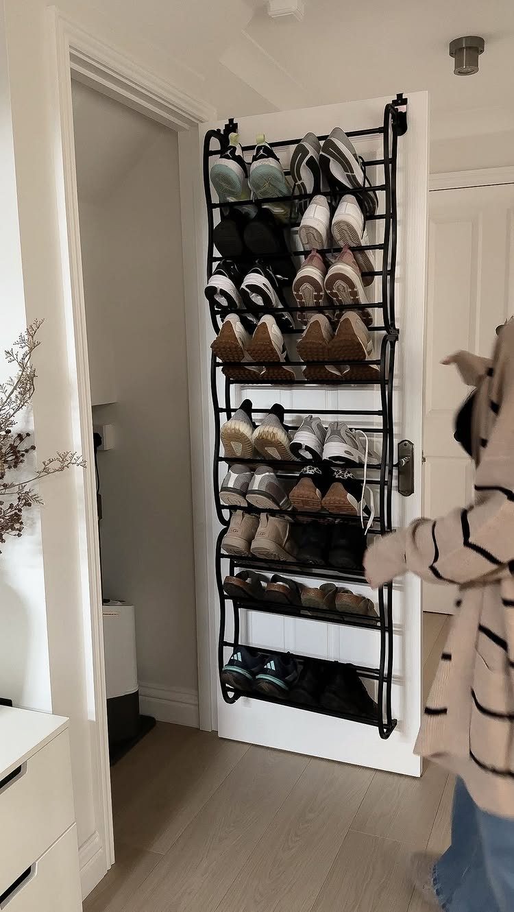Black metal over-the-door shoe organizer filled with footwear on a white door.